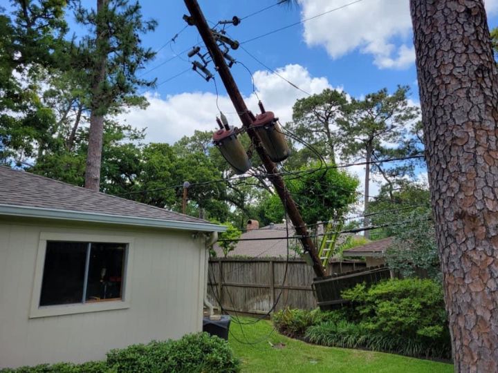 A downed power line and electricity pole in the backyard of a white house.