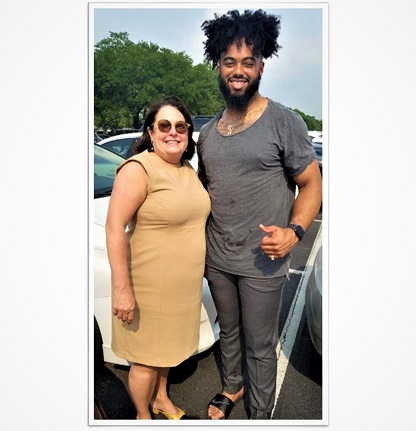 A dark-haired woman in tan dress stands next to a tall bearded man in grey clothing