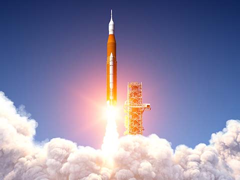 The NASA Space Launch System lifting off from its launch pad. A large plume of exhaust fills the bottom portion of the picture.