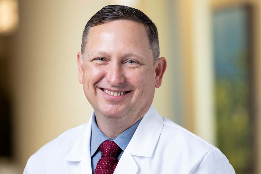 Portrait of a man smiling with short brown hair wearing a white lab coat.