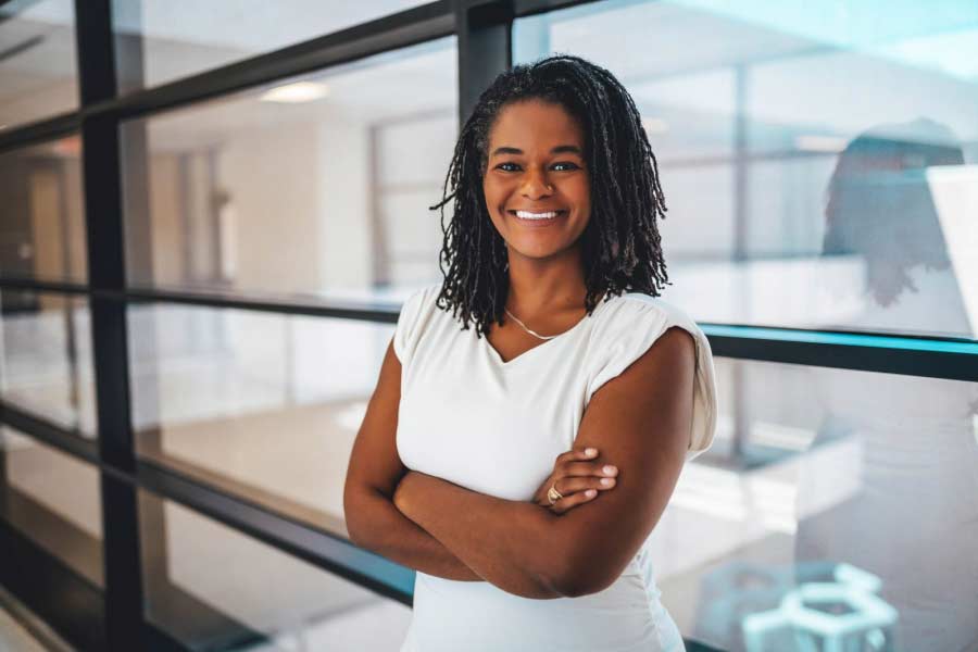 Portrait of a Black woman smiling with her arms crossed in a white sleeveless blouse.