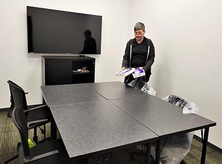 A woman places two small product boxes onto an table with empty chairs.