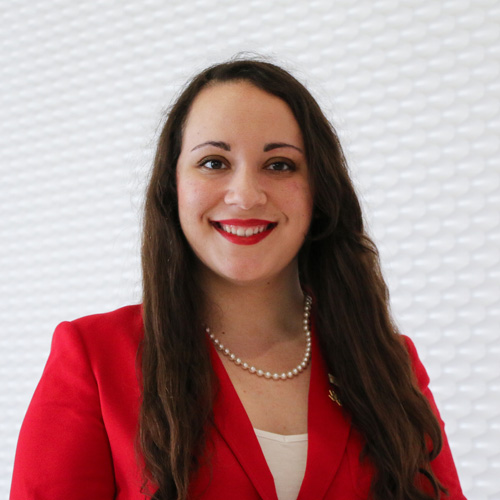 Portrait of a white woman smiling with brown mid-back length hair wearing a red business suit